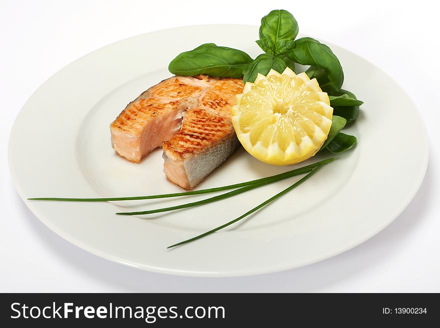 Roasted salmon steak decorated with lemon and basil on plate