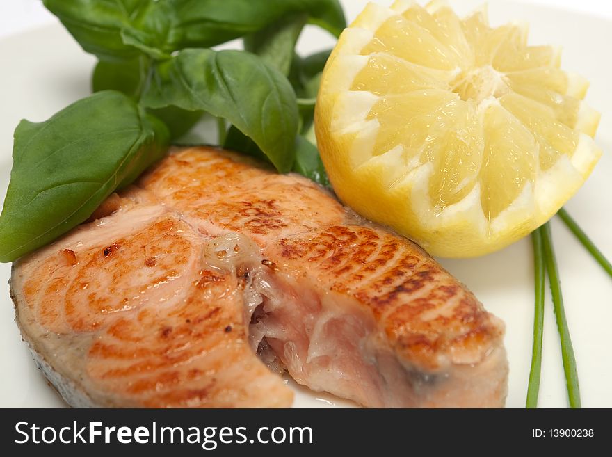 Roasted salmon steak decorated with lemon and basil on plate