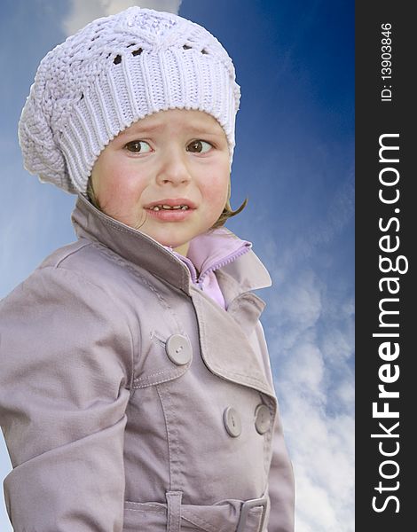 The little girl with tear-stained eyes in a cap and a raincoat with a belt. The little girl with tear-stained eyes in a cap and a raincoat with a belt