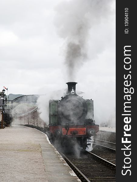A vertical image of a steam locomotive leaving the station with lots of smoke and steam. A vertical image of a steam locomotive leaving the station with lots of smoke and steam