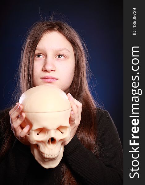 Portrait of teenager girl holding anatomical model of human skull. Black background with blue highlight. Portrait of teenager girl holding anatomical model of human skull. Black background with blue highlight