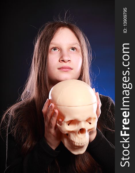 Portrait of teenager girl holding anatomical model of human skull. Black background with blue highlight. Portrait of teenager girl holding anatomical model of human skull. Black background with blue highlight