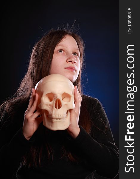 Portrait of teenager girl holding anatomical model of human skull. Black background with blue highlight. Portrait of teenager girl holding anatomical model of human skull. Black background with blue highlight