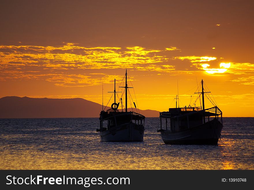 Two boats as silhouettes while the sun's setting behind clouds. Two boats as silhouettes while the sun's setting behind clouds.