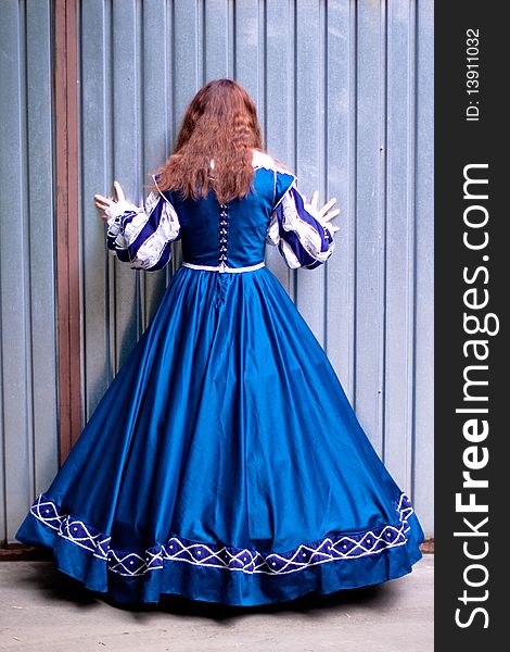 Girl in medieval blue dress standing near metal wall. Girl in medieval blue dress standing near metal wall
