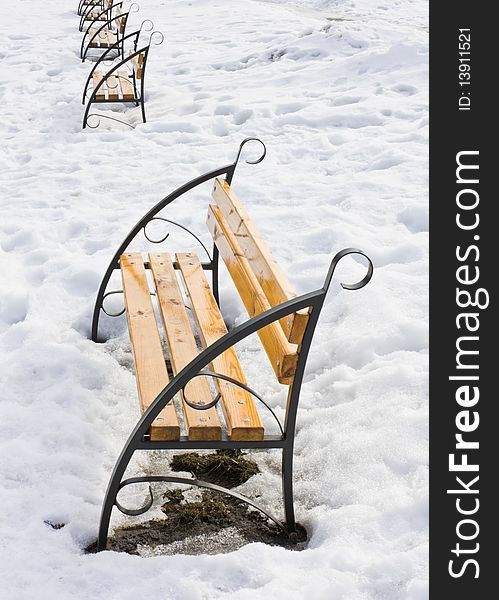 Light brown wooden benches on snow in the park