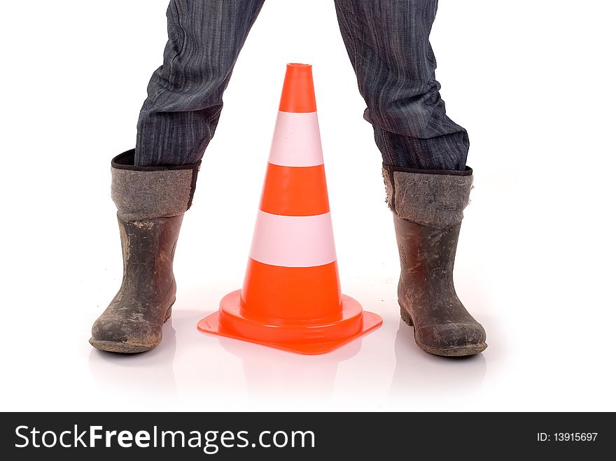 Safety cone placed between builder's legs clad in rubber boots. Safety cone placed between builder's legs clad in rubber boots.