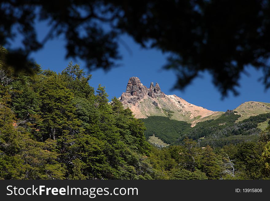 The view of a mountain on a beautiful blue sky framed with the trees around. The view of a mountain on a beautiful blue sky framed with the trees around.