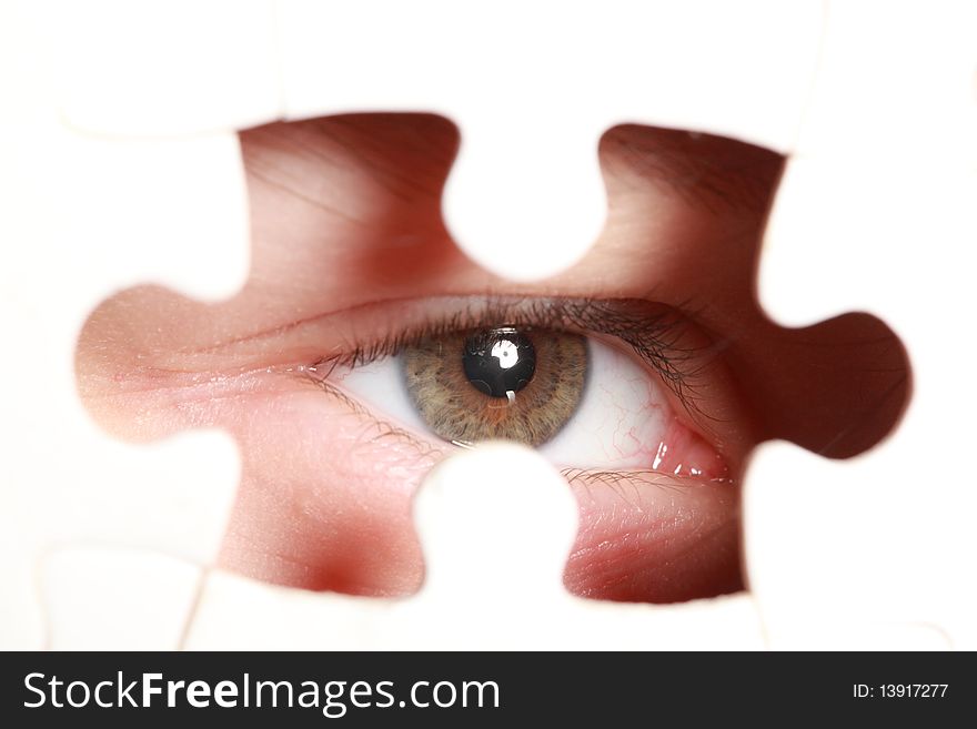 Human eye looking out through the hole in jigsaw puzzle