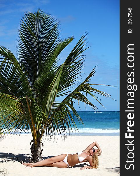 Young female in white bikini enjoying sunny day under palm tree on the tropical beach. Young female in white bikini enjoying sunny day under palm tree on the tropical beach