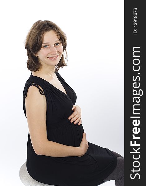 Beautiful young pregnant woman smiling and sitting in black dress on white background. Beautiful young pregnant woman smiling and sitting in black dress on white background