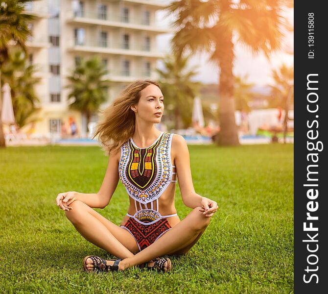 Young beautiful girl wearing fashion swimsuit monokini with a national african ethnic pattern sitting on a lawn