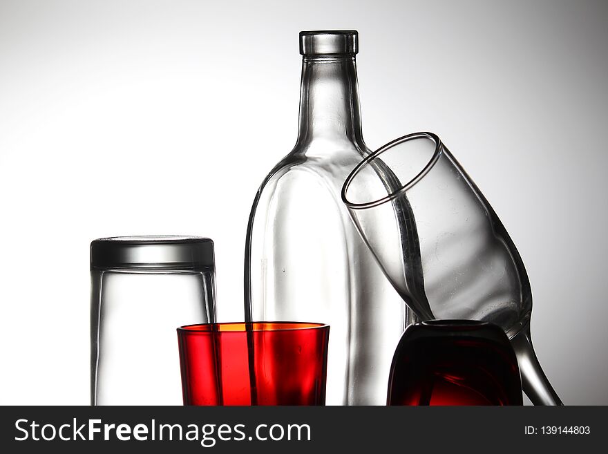 A transparent bottle and red glasses against bright background