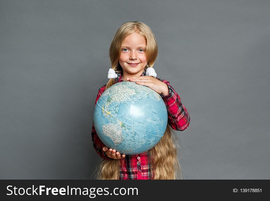 Little girl with two ponytails studio standing isolated on grey wall holding globe traveling around the world looking camera smiling positive. Little girl with two ponytails studio standing isolated on grey wall holding globe traveling around the world looking camera smiling positive
