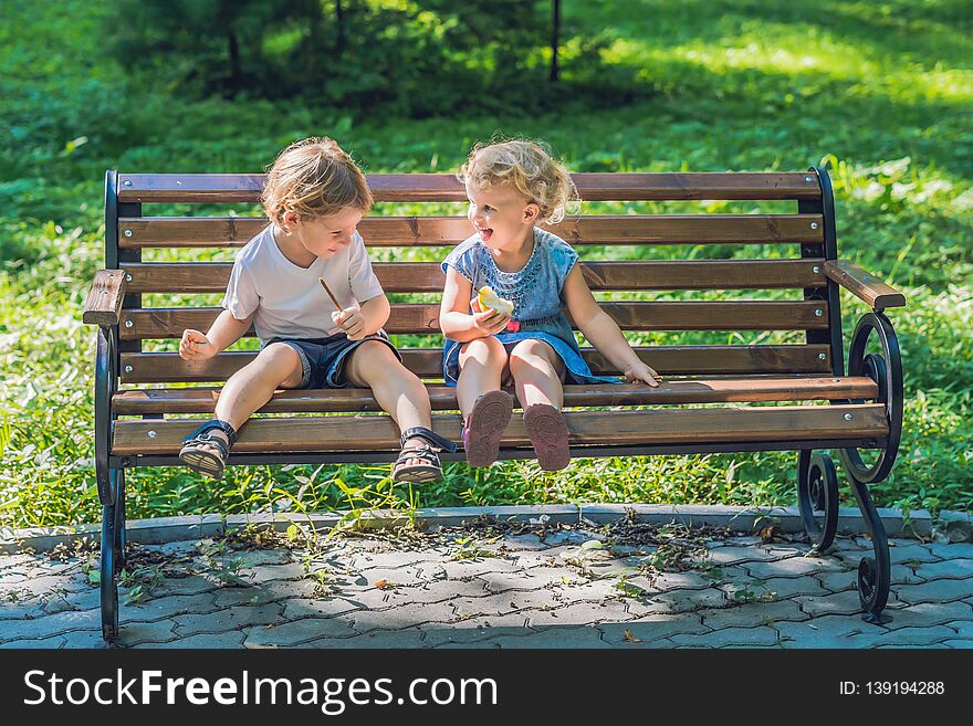 Toddlers boy and girl sitting on a bench by the sea and eat an apple