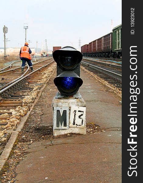 Railway traffic lights burning blue, a railway worker in overalls is on rails. Railway traffic lights burning blue, a railway worker in overalls is on rails