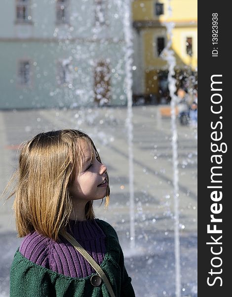 Caucasian joyful little girl visiting urban square with beautiful fountain. Caucasian joyful little girl visiting urban square with beautiful fountain