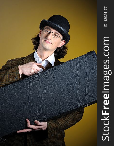 Portrait of young english retro gentleman in bowler hat holding suitcase as a luggage. yellow background. Portrait of young english retro gentleman in bowler hat holding suitcase as a luggage. yellow background