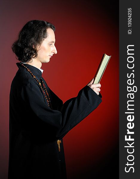 Conceptual portrait of Praying priest with wooden cross reading Holy Bible. red background. Conceptual portrait of Praying priest with wooden cross reading Holy Bible. red background