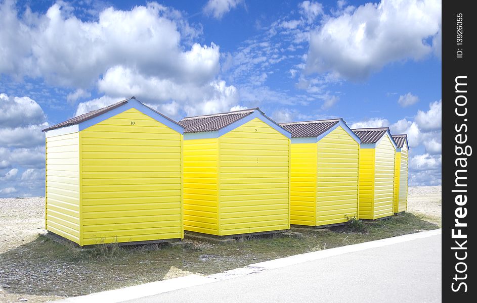 Four yellow beach huts on teh edge of a sandy beach.