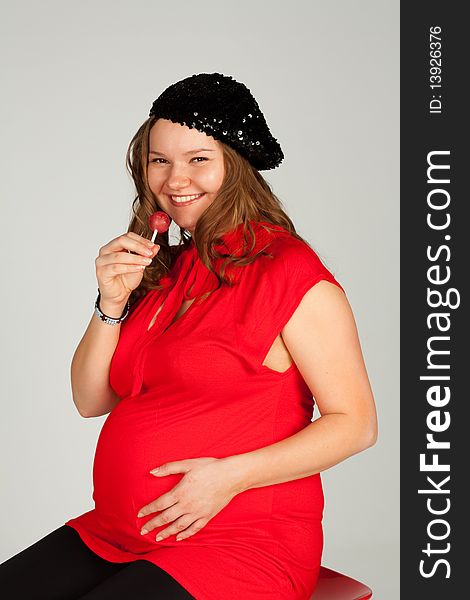 A pregnant woman in a red shirt, black beret and black leggings with candy in hand. A pregnant woman in a red shirt, black beret and black leggings with candy in hand