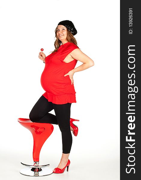 A pregnant woman in a red shirt, red shoes and black leggings is leaning on one leg