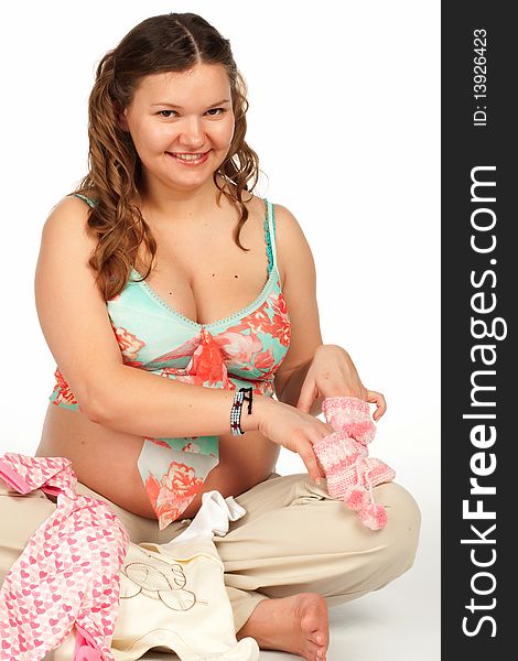 Beautiful happy smiling pregnant woman holding a rose baby shoes and bodysuit next to her bare belly, isolated. Beautiful happy smiling pregnant woman holding a rose baby shoes and bodysuit next to her bare belly, isolated