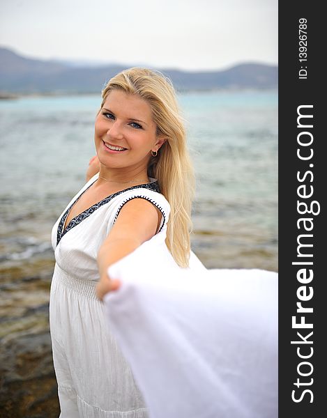 Young beautiful romantic woman in white dress dancing with shawl near blue sea