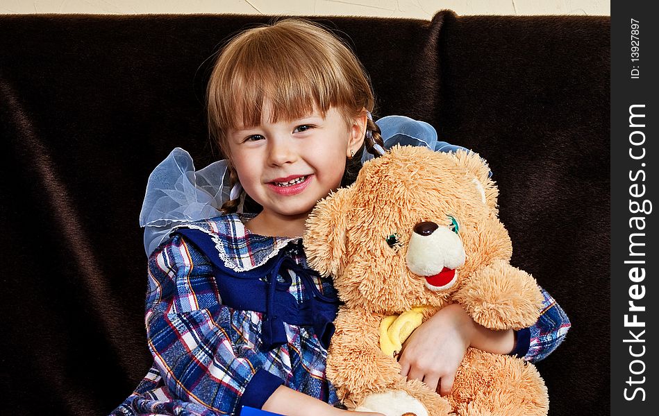 Little girl embraces bear cub sitting on sofa