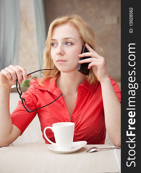Young blond girl in cafe is drinking coffee and speaking by mobile phone