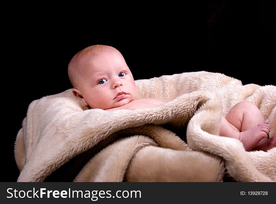 3 Month old baby lying naked on a fluffy blanket on a black background