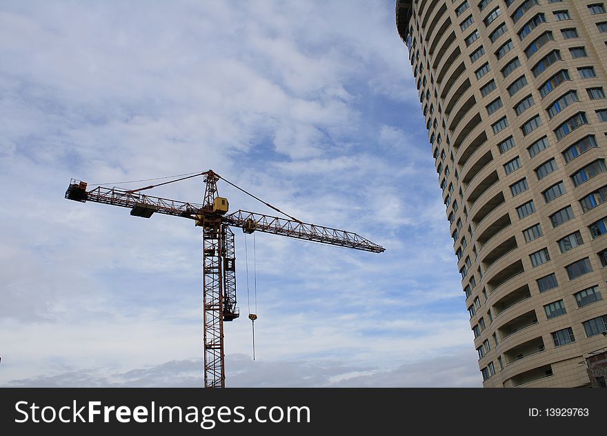 Crane and state of the art multi-storey building on a background of blue sky with clouds, the construction of residential house. Crane and state of the art multi-storey building on a background of blue sky with clouds, the construction of residential house