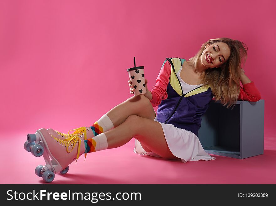 Young woman with retro roller skates and cup of drink