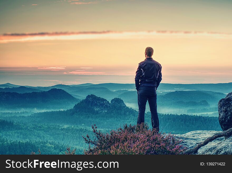 Man tourist traveler standing on cliff of mountain and looking to sunset, against backdrop of hills. Concept active recreation in mountains