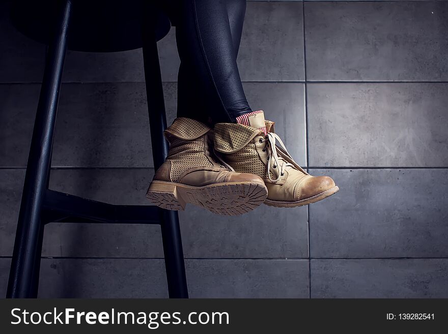 Dark low section of woman wearing boots sitting at bar counter in cafe