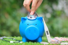 Woman Using Stethoscope To Check Blue Piggy Bank With Thermometer And Medicine On Natural Green Background,Save Money For Medical Stock Photography