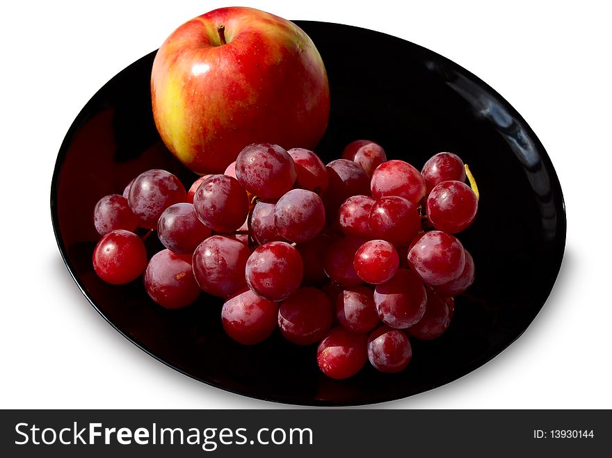 Red grapes and apple on a black plate isolated on a white background. Red grapes and apple on a black plate isolated on a white background