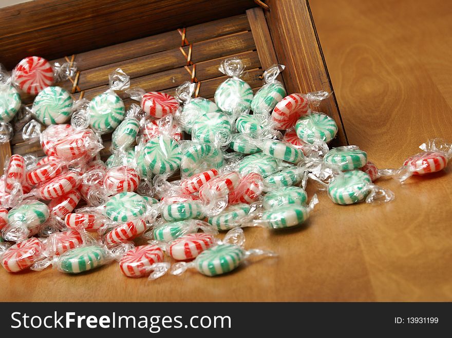 A closeup of peppermint swirl candies spilling from a wooden container. A closeup of peppermint swirl candies spilling from a wooden container.