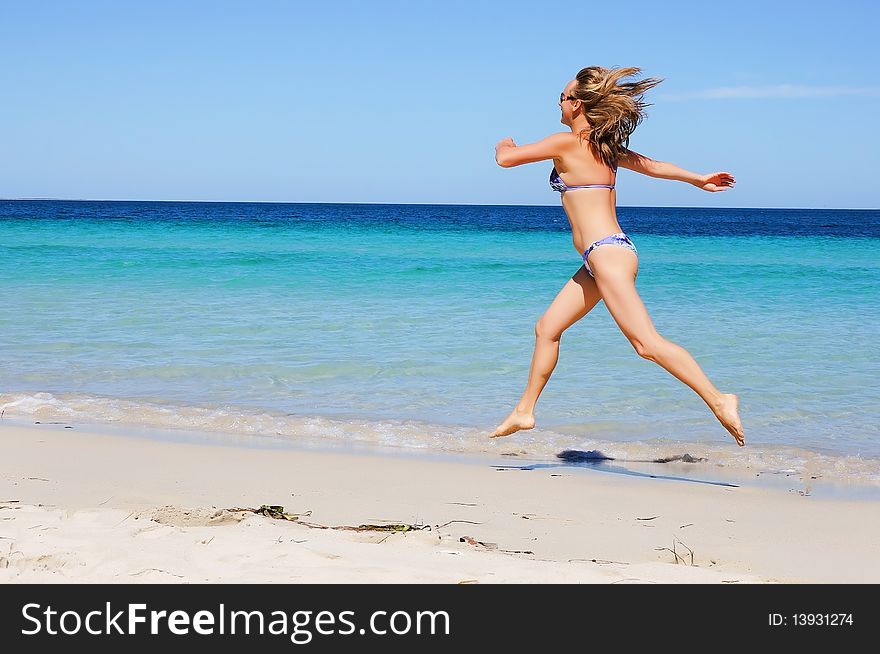 Charming tanned girl running across a sandy beach along the ocean