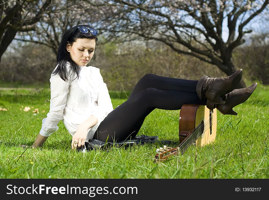 The beautiful girl lies on a green grass with a guitar. The beautiful girl lies on a green grass with a guitar