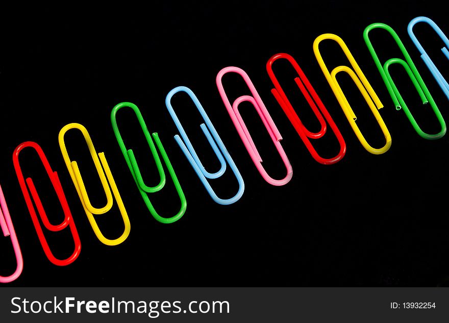 Bunch of paper clips on black background. Loose paper clips in background.