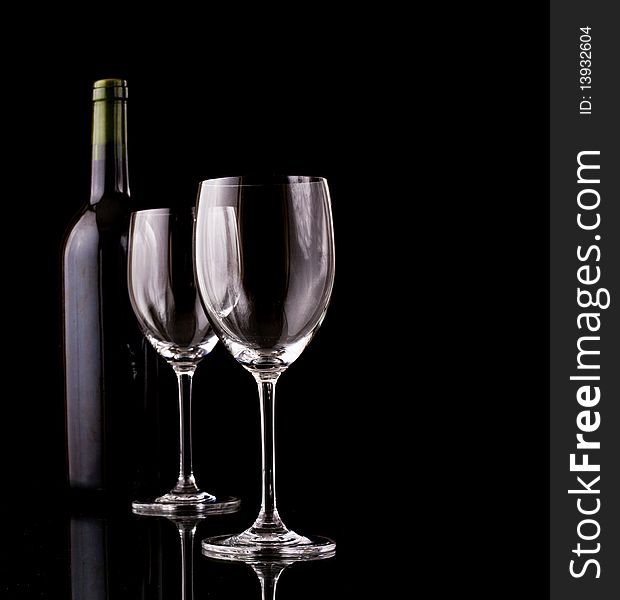 Bottle of red wine and empty glasses wrapped in a dark ambiance of a cellar with black background. Bottle of red wine and empty glasses wrapped in a dark ambiance of a cellar with black background