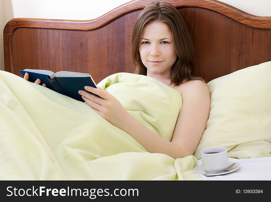 Young beautiful woman with book and cup of coffee in the bed. Young beautiful woman with book and cup of coffee in the bed