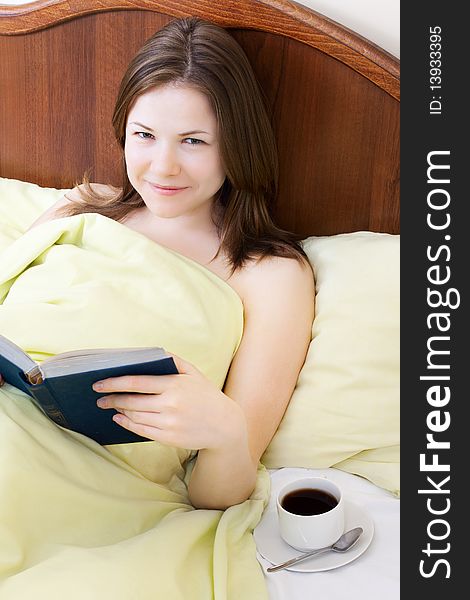 Young beautiful woman with book and cup of coffee in the bed. Young beautiful woman with book and cup of coffee in the bed