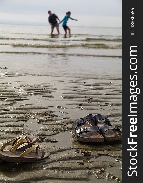 A couple who ran to the beach left their sandles on the beach to play in the water. A couple who ran to the beach left their sandles on the beach to play in the water