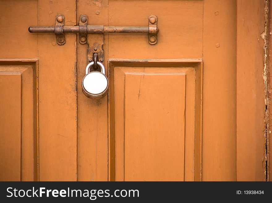 Locked dark orange door of a very old house seems quite durable and strong. Locked dark orange door of a very old house seems quite durable and strong