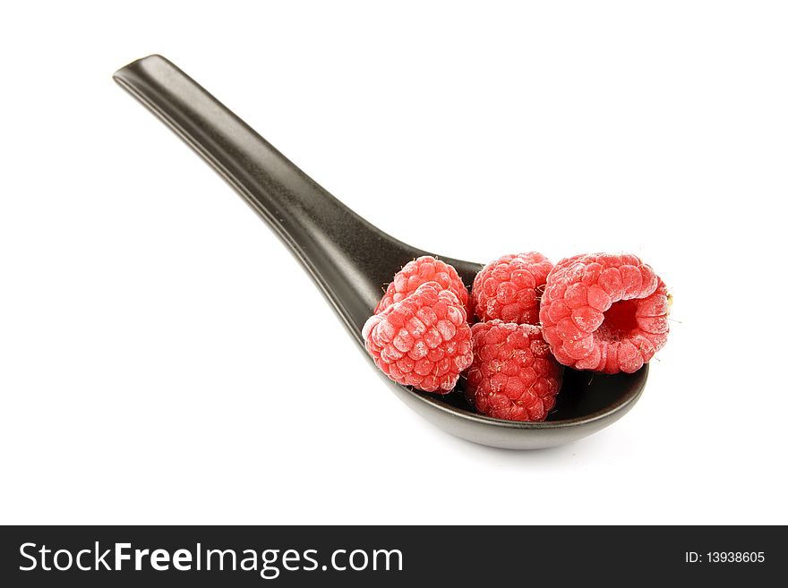 Red ripe frozen raspberries on a small black spoon with a reflective white background. Red ripe frozen raspberries on a small black spoon with a reflective white background