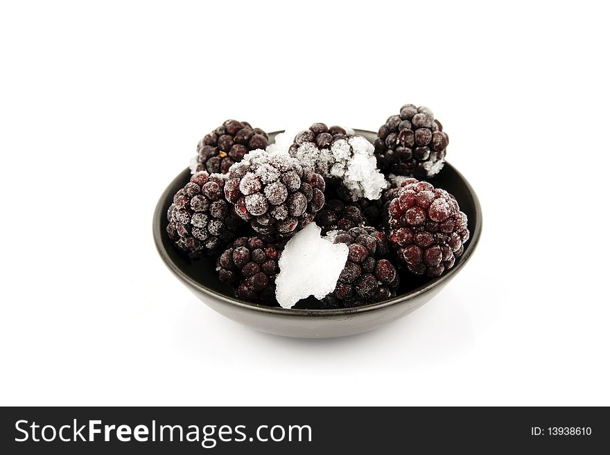 Ripe frozen blackberries in a small black bowl on a reflective white background. Ripe frozen blackberries in a small black bowl on a reflective white background