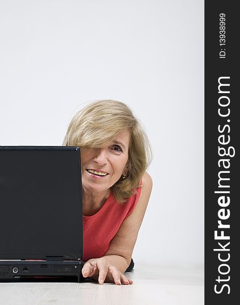Portrait of blond mature woman hidden half behind laptop smiling for you,copy space for text message in right part of image,see more in People on couch or wooden floor. Portrait of blond mature woman hidden half behind laptop smiling for you,copy space for text message in right part of image,see more in People on couch or wooden floor
