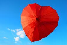 Red, Scarlet Umbrella In The Shape Of Heart Against Blue Sky On Clear, Sunny Day. Valentine`s Day Concept Stock Photo
